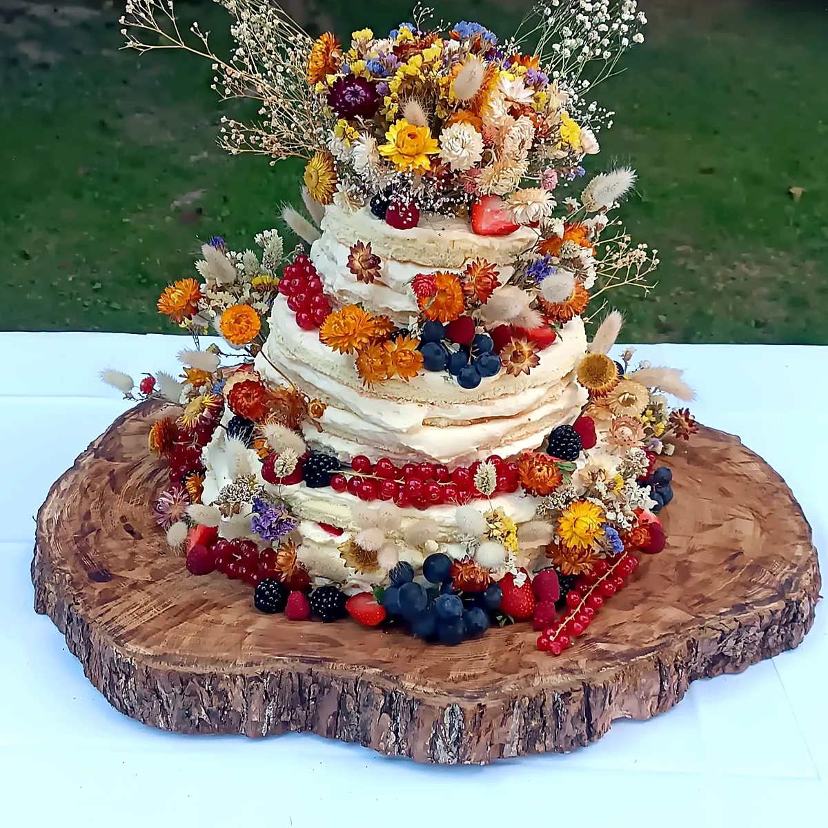 Naked Cake mit Beeren und Blüten auf der Holzscheibe